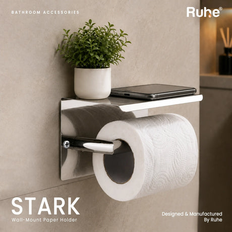 Stark SS 304 toilet roll holder with mobile shelf on a tiled bathroom wall, with a phone and small plant pot